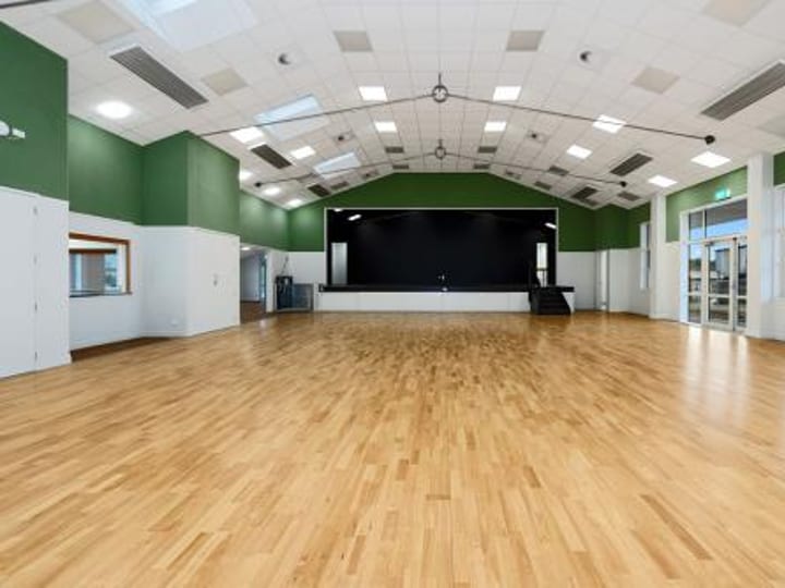 Large hall with vaulted ceiling, green walls, raised stage and timber floor