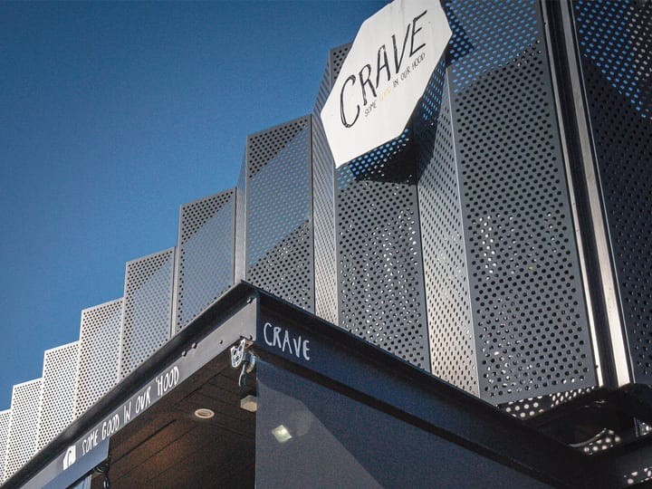 Close-up of angular perforated metal cladding on building exterior with signage, blue sky above