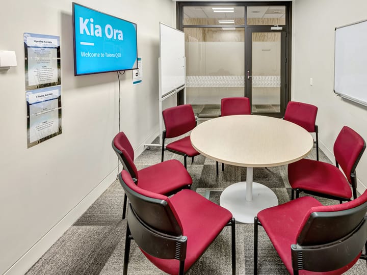 Small meeting room with round table, red chairs, TV screen, and whiteboard