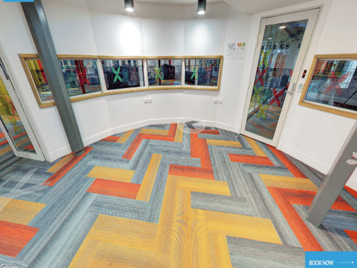 White curved interior corridor with colourful herringbone carpet tiles and framed windows