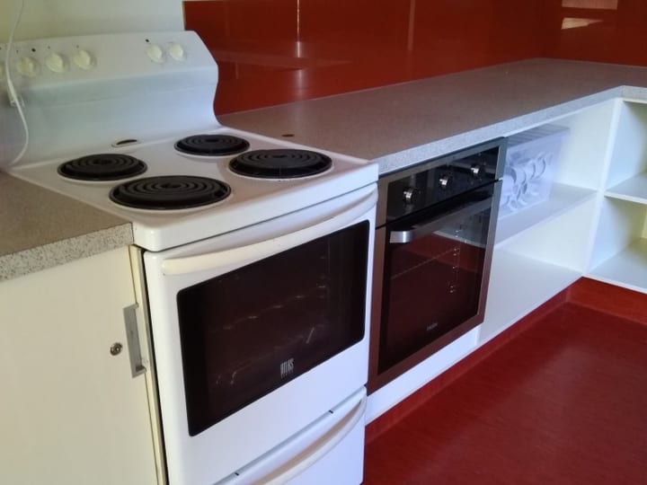 Small hall kitchen with white electric stove, wall oven, and red splashback
