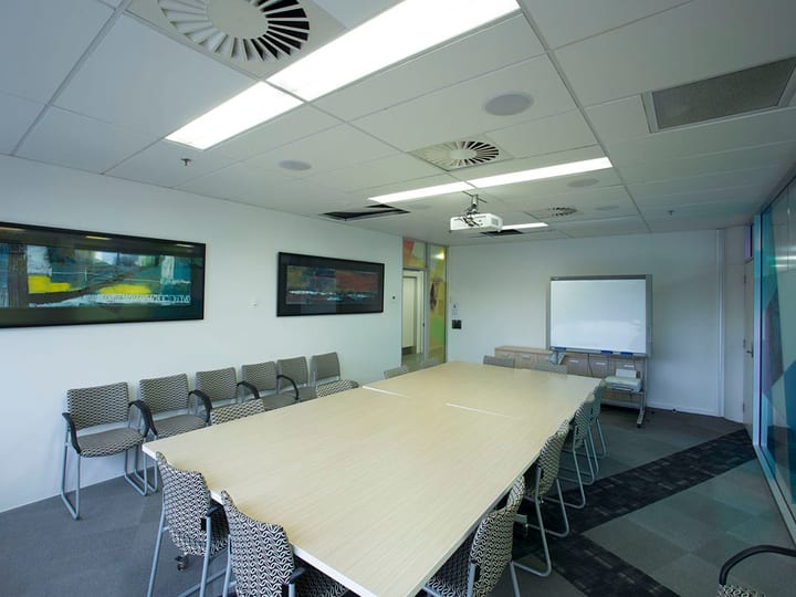 Meeting room with long timber table, patterned chairs, projector, and framed artworks