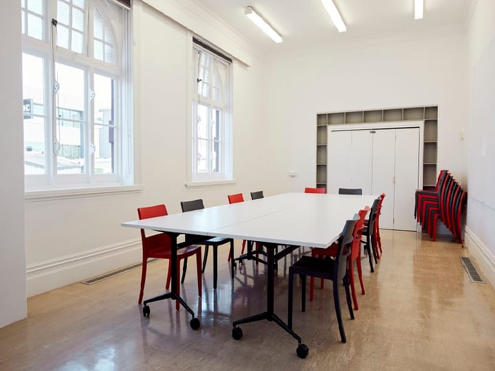 White meeting room with large windows, long folding table, red and dark chairs, polished floor