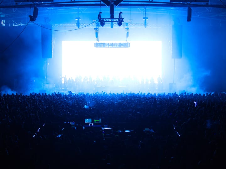 Large indoor arena with blue stage lighting and full crowd