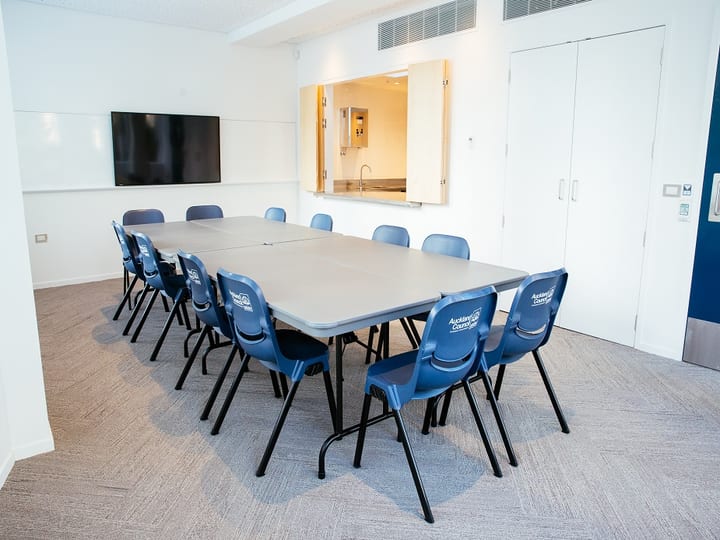 Meeting room with boardroom table, blue chairs, screen and servery hatch