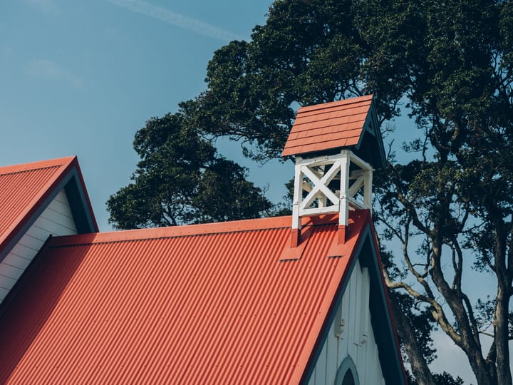 Close-up of timber church roofline with red corrugated iron and small bell tower against blue sky