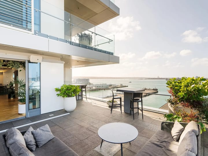 Rooftop terrace with grey sofas and planters, glass balustrade, and harbour and cityscape view