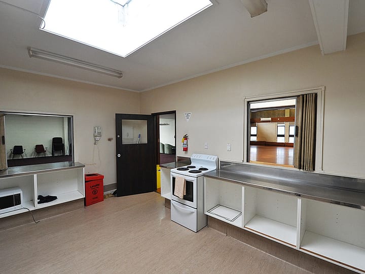 Hall kitchen with stainless bench, stove and skylight, opening to main hall