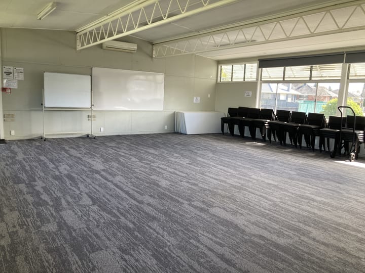 Plain hall with whiteboards, stacked black chairs and large windows