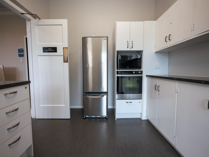 Kitchenette with stainless steel fridge, built-in oven, microwave and white cabinetry