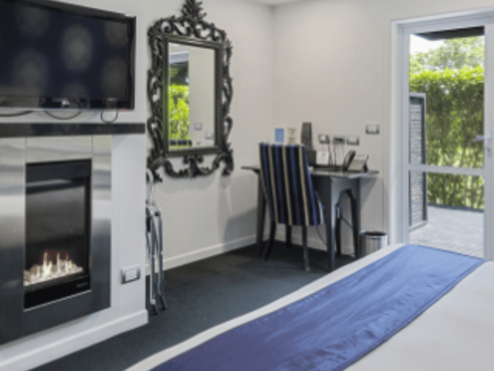 White-painted bedroom with gas fireplace, ornate mirror, wall-mounted television, and glass door to garden