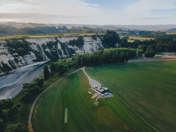 Aerial view of a small building set on open green farmland beside white cliffs and a river