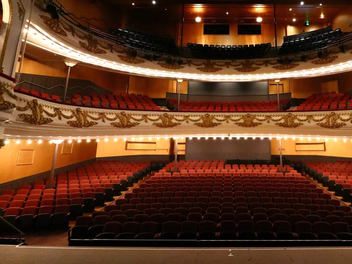 Ornate theatre auditorium with red seating, balcony and decorative plasterwork