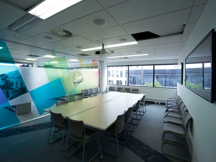 Meeting room with long table, chairs, colourful graphic glass wall, and windows