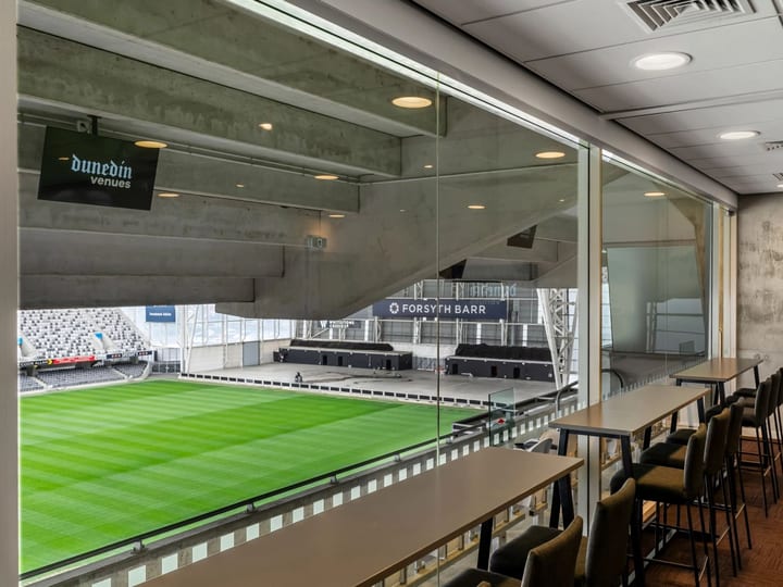 Stadium suite with high bar tables and glass wall overlooking stadium seating and pitch