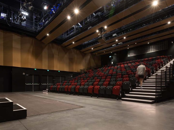 Tiered auditorium with red and dark seats, stage, and overhead rigging