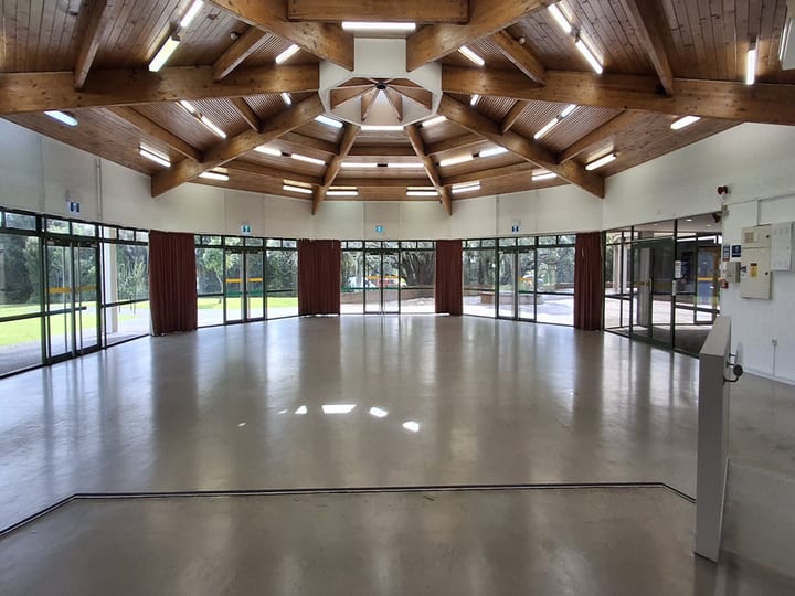 Circular hall with large timber roof beams, concrete floor, and glass walls to gardens