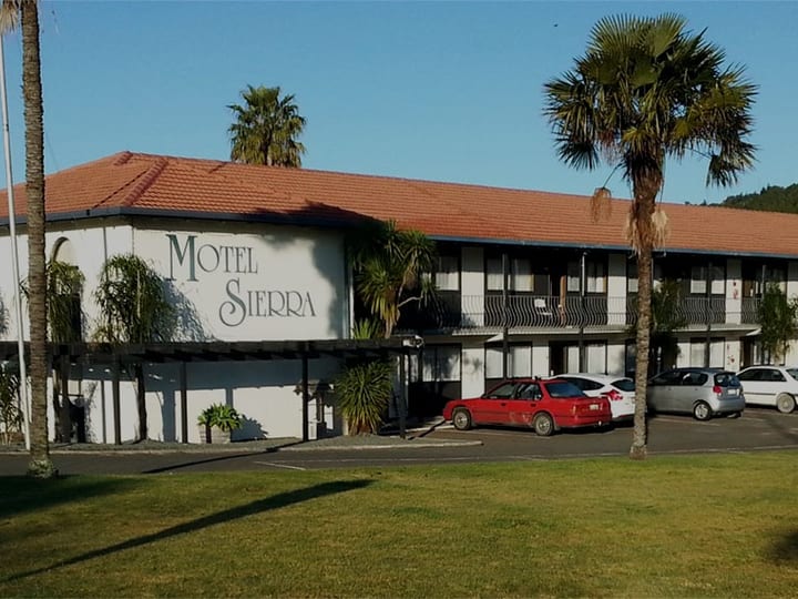 Two-storey motel building with parking area and palm trees in foreground