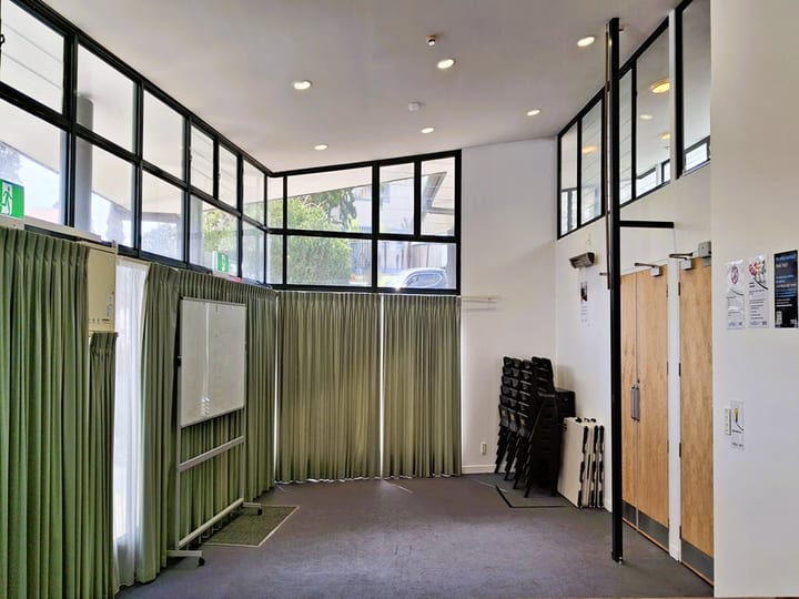 Smaller meeting room with green curtains, whiteboard on wheels, stacked chairs and high clerestory windows