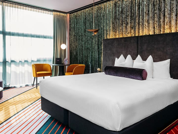 Hotel room with large bed, teal-toned feature wall and yellow accent chairs