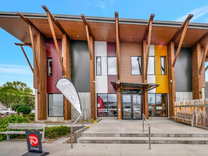 Two-storey community centre exterior with angled timber columns, coloured cladding panels, and covered entry