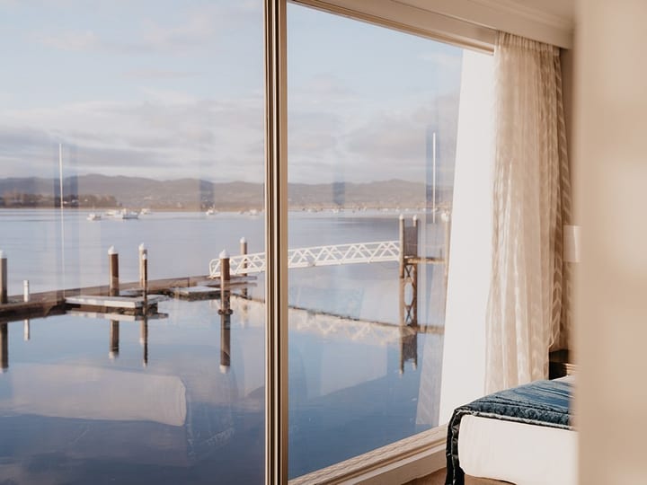 Guest room window view of harbour jetty, calm water, and hills at dawn