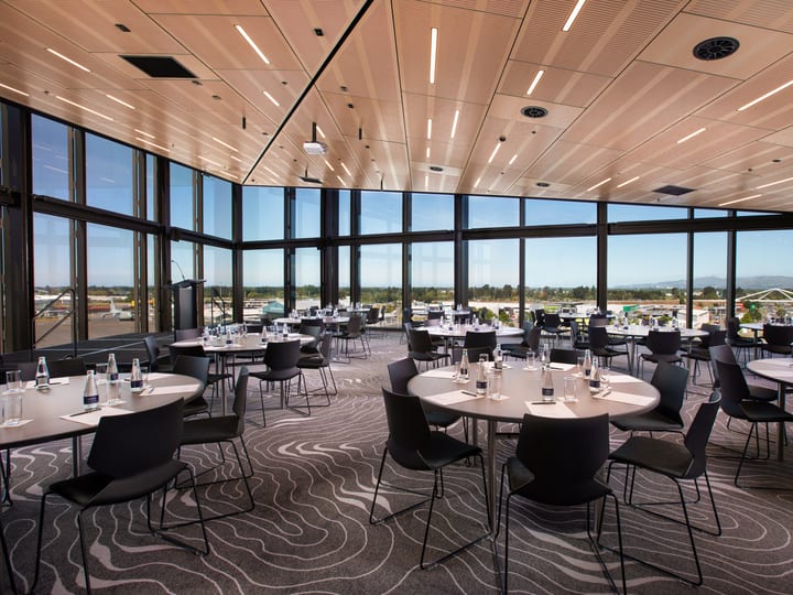 Light timber ceiling event room with round tables and black chairs, floor-to-ceiling windows and open views