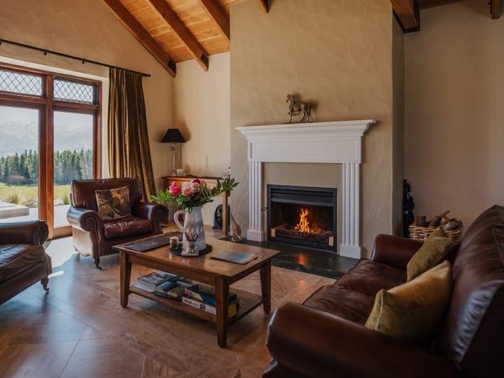 Vaulted timber-beam lounge with white fireplace, leather armchairs and mountain view through windows