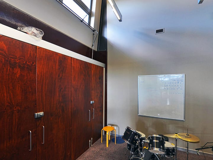 Small carpeted room with timber panel wall, whiteboard, and drum kit in corner