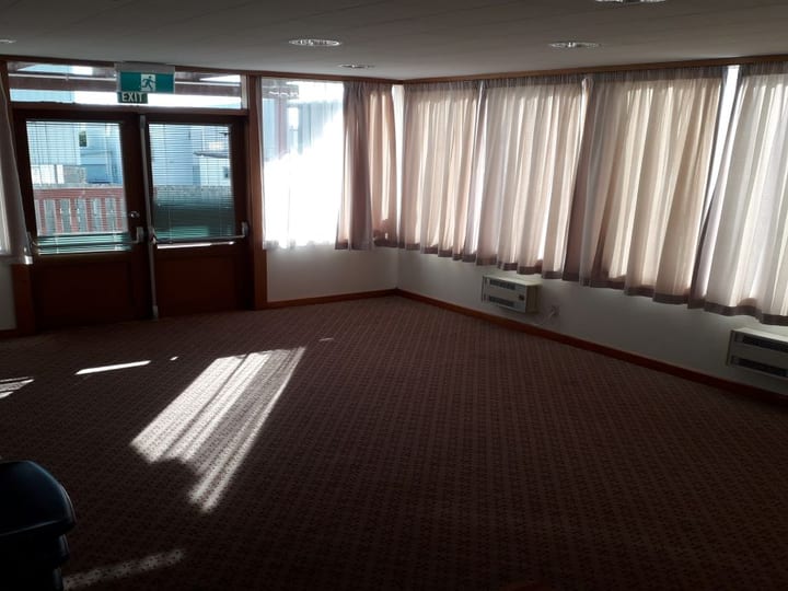 Hall room with whiteboard, stacked chairs, and interior window to adjoining space