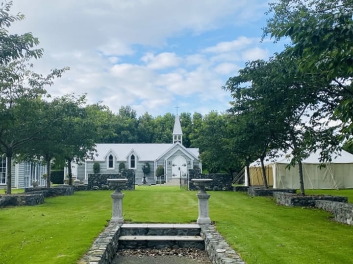 Chapel viewed across garden with stone walls and lawn pathway