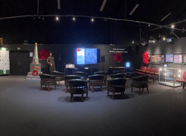 Dim exhibition room with leather chairs, memorial display and wall screen