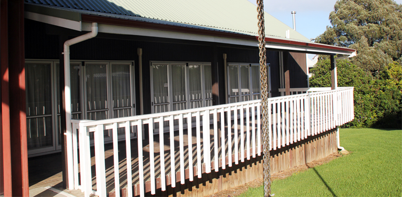 Single-storey dark-clad hall with covered deck and white timber railing