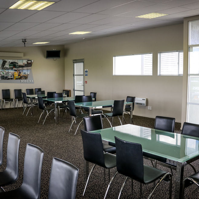 Function room with glass-topped tables and black chairs under a ceiling of fluorescent lights