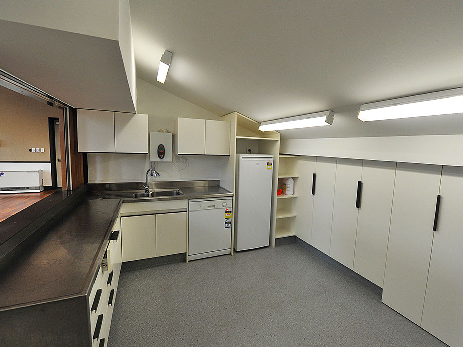 Catering kitchen with white cabinetry, stainless benches, dishwasher, and fridge