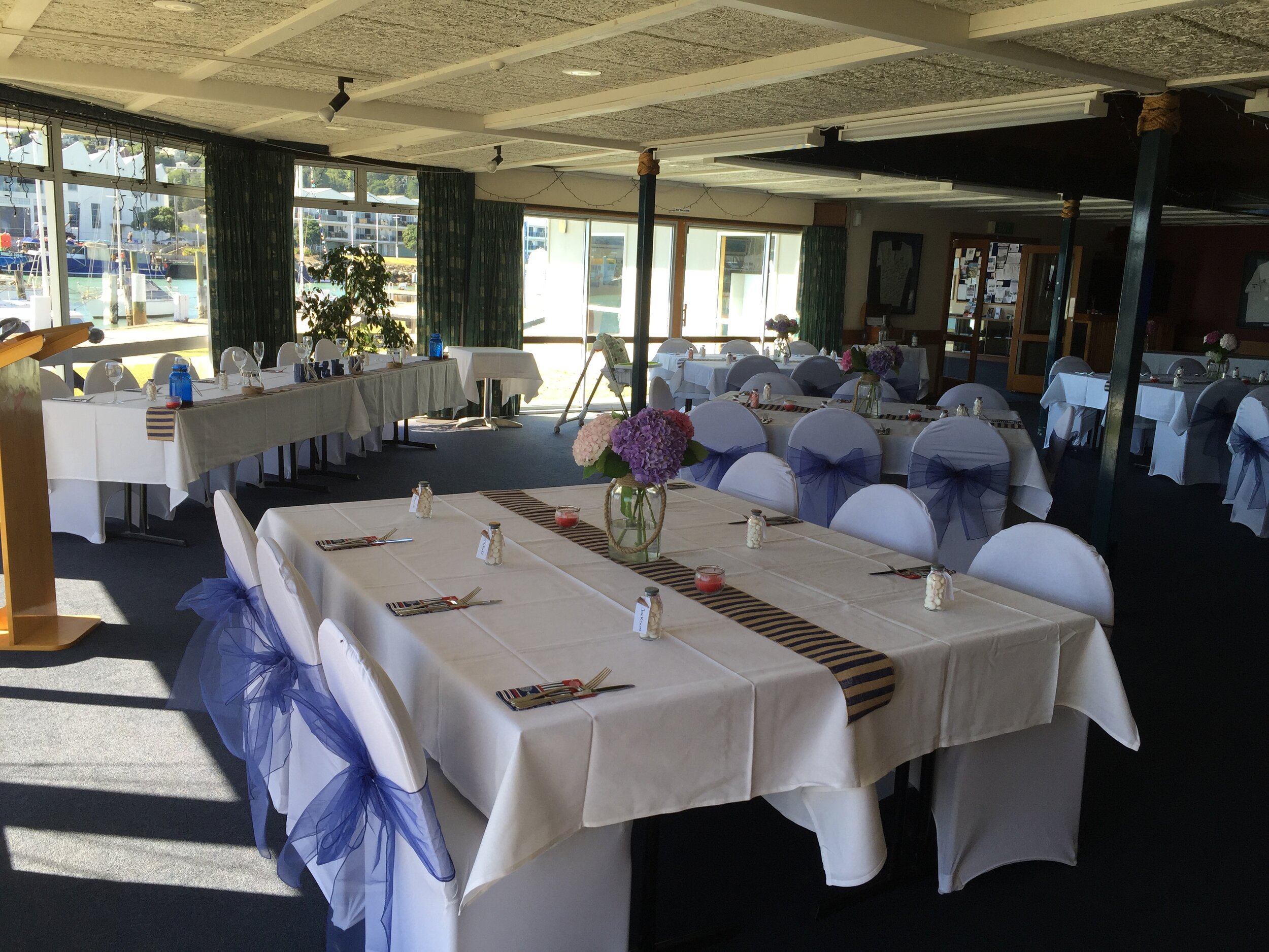 Function room set with white-clothed tables, chair covers and windows to a marina