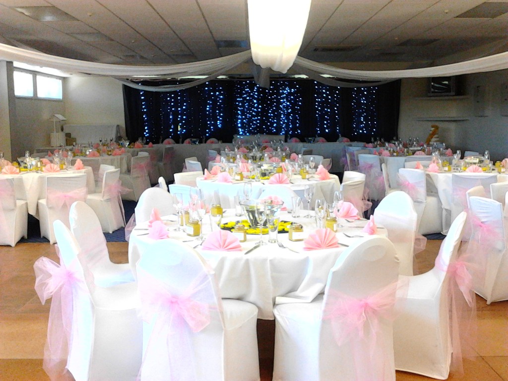 Hall set with round tables, white chair covers with pink bows and draped ceiling