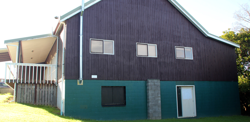 Two-storey dark-clad hall exterior with lawn and neighbouring outbuilding
