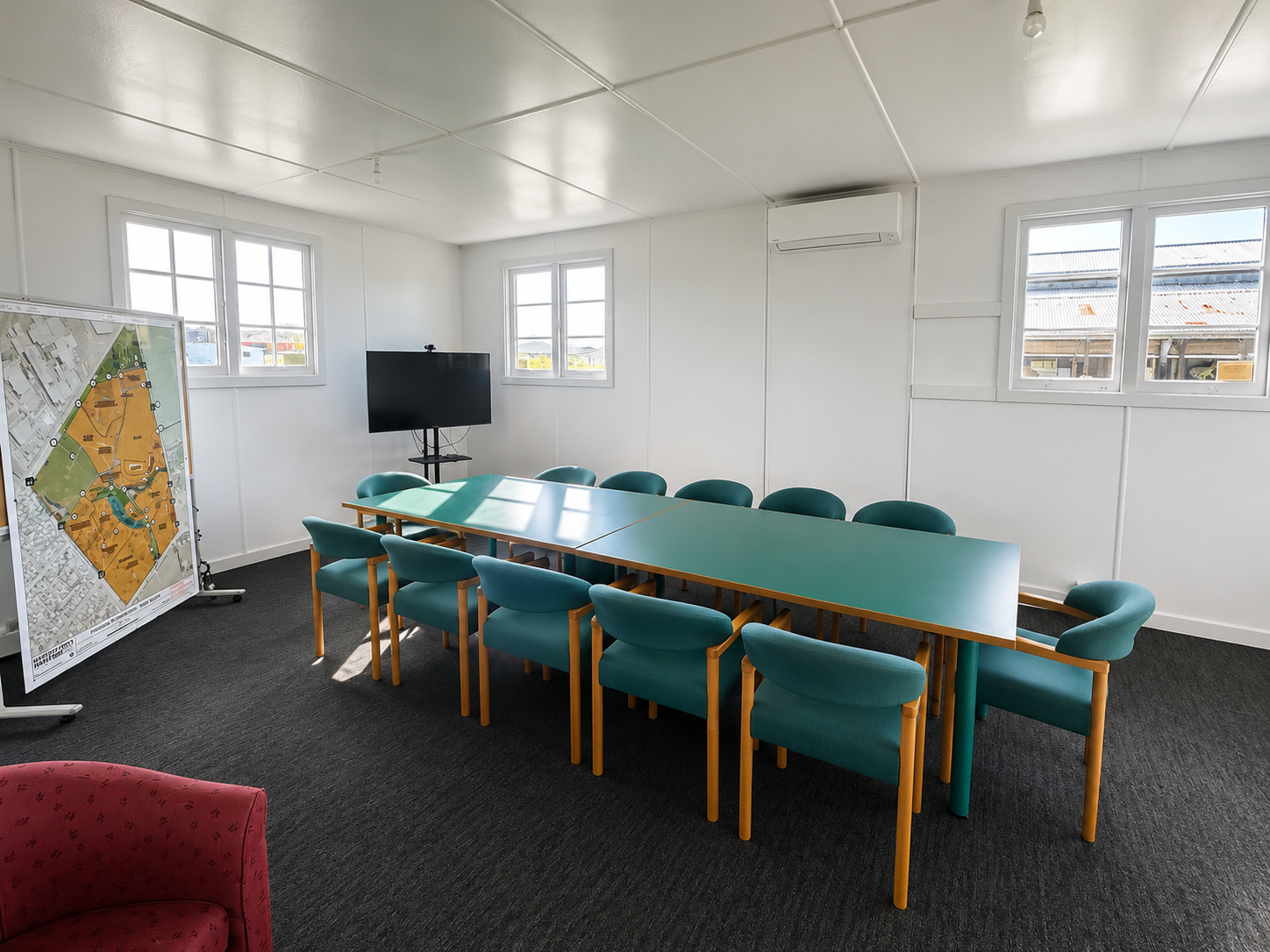 Meeting room with a long green table, teal chairs, wall screen and site map