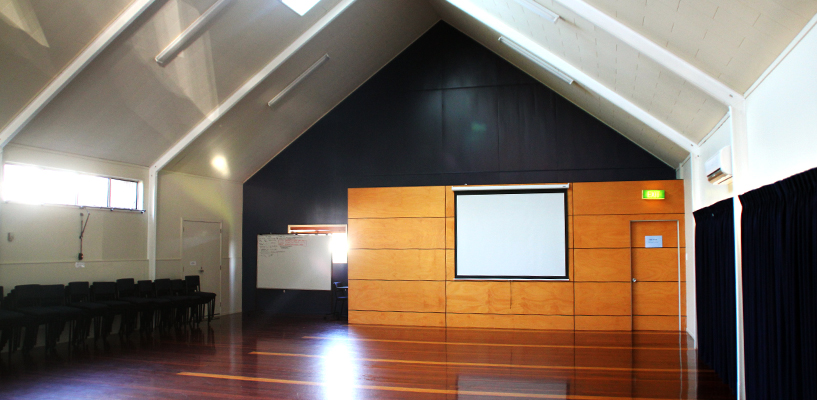Hall interior with vaulted ceiling, polished timber floor, and projection screen on timber feature wall