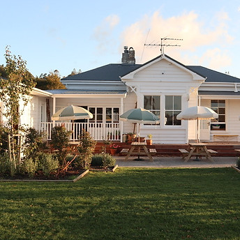 White timber cottage exterior with verandah, outdoor tables and umbrellas, small lawn garden