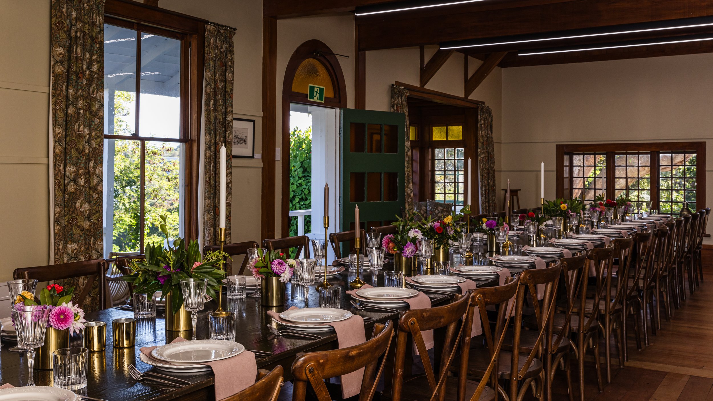 Long set dining table with flowers, candles and wooden chairs in a timber-trimmed room