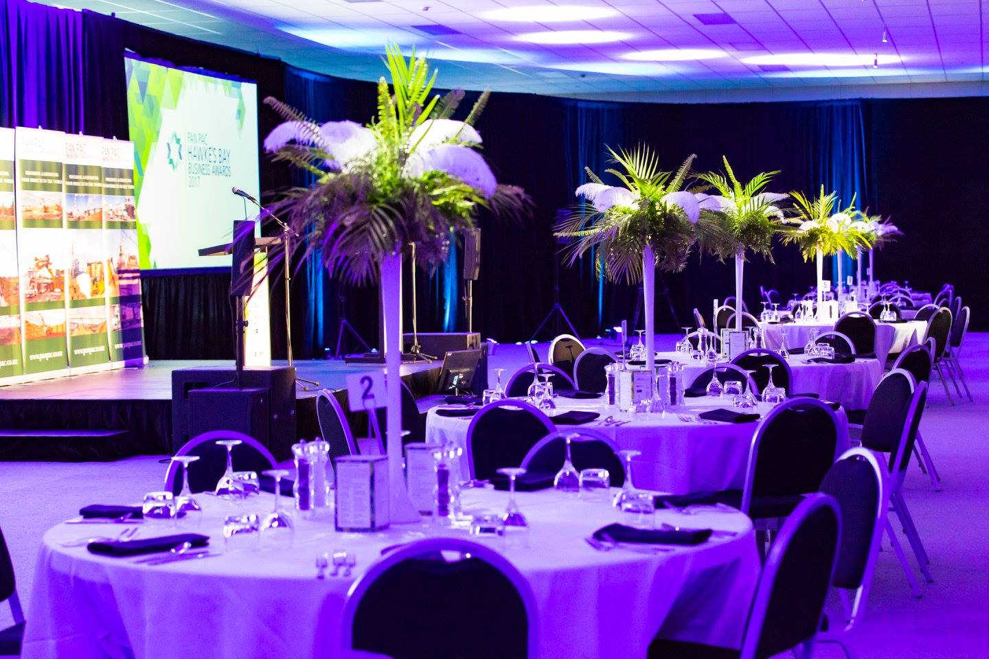 Large function room with round tables, tall centrepieces and stage with screen