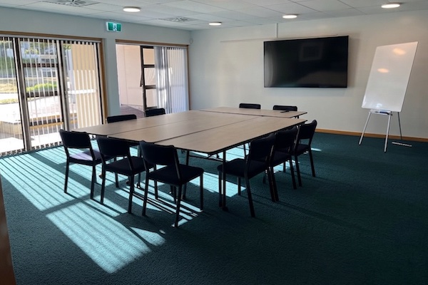 Meeting room with joined tables, black chairs, wall screen and whiteboard