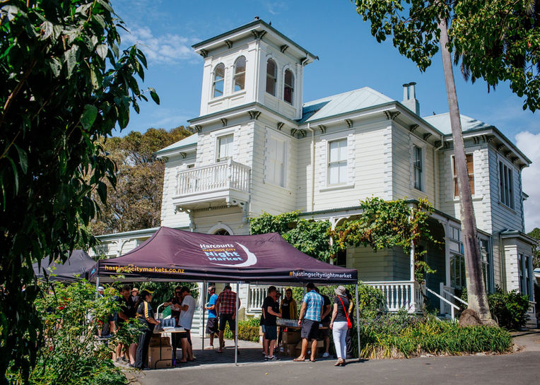 Two-storey white weatherboard house with a square tower, a market tent and visitors in front