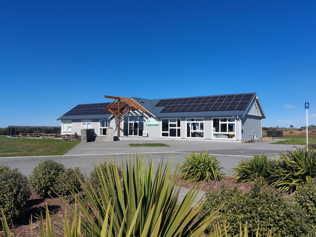 Low-profile building with solar panels on roof, timber entrance and native plantings